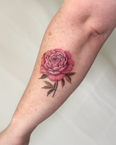 A realistic color rose tattoo on the forearm, featuring delicate petals and leaves in a botanical style — by Melanie Benoit, los angeles