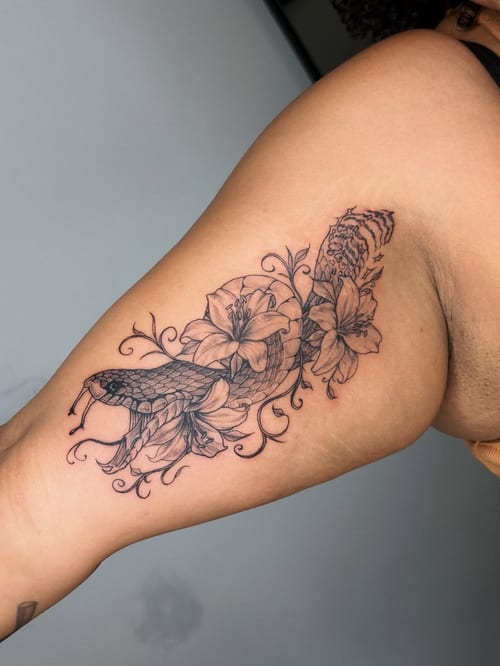 A delicate black and grey tattoo of a snake intertwined with flowers on the inner arm, featuring fine line details — by lunayflorestattoo, los angeles