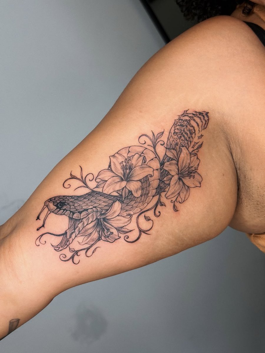 A delicate black and grey tattoo of a snake intertwined with flowers on the inner arm, featuring fine line details — by lunayflorestattoo, los angeles
