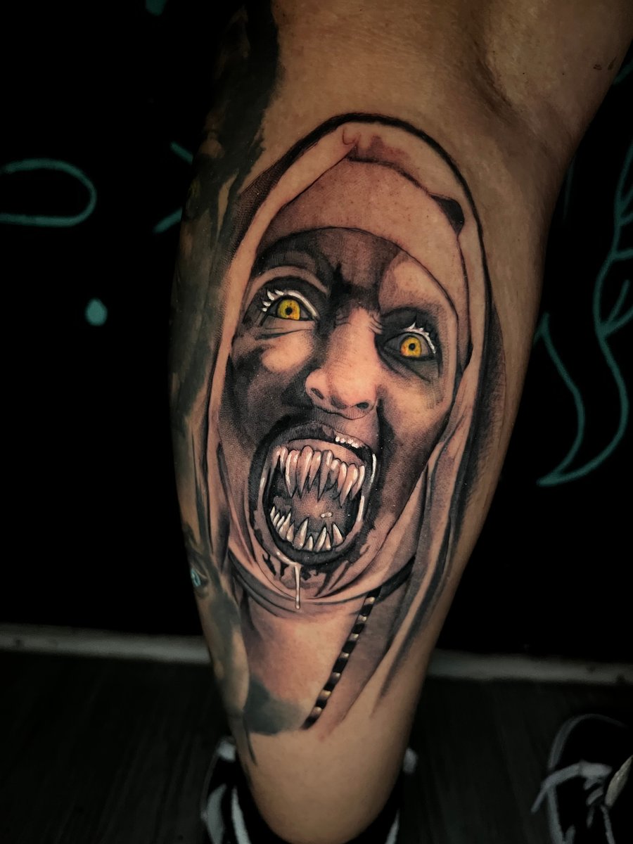 A realistic horror-themed tattoo on the calf depicting a demonic face with intense yellow eyes and sharp teeth, using a mix of color and black and grey shading — by Josue Bravo, los angeles