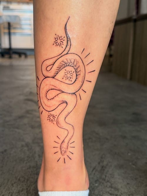 A minimal linework snake tattoo on the calf with simple black outlines and minimalistic design elements — by Kiera Garvin, los angeles