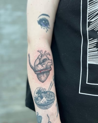 An anatomical heart with a rope wrapped around it, done in black and grey on the forearm with a graphic style — by Dylan Aiello, los angeles