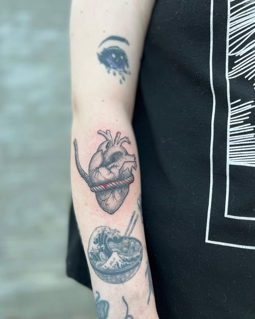 An anatomical heart with a rope wrapped around it, done in black and grey on the forearm with a graphic style — by Dylan Aiello, los angeles