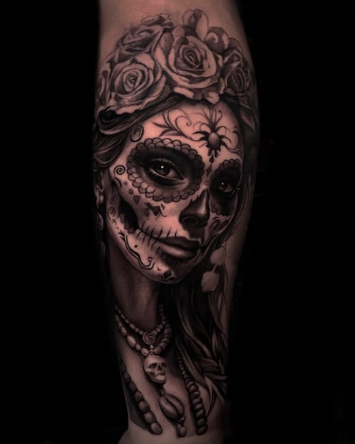 A detailed black and grey sugar skull woman portrait on the forearm, featuring roses and intricate facial designs — by Vladimir Kozachenko, los angeles