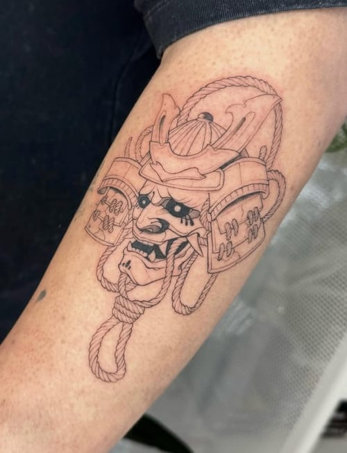 A detailed black and grey linework tattoo of a samurai helmet on the forearm, showcasing intricate design and shading — by otaybeatdown, los angeles