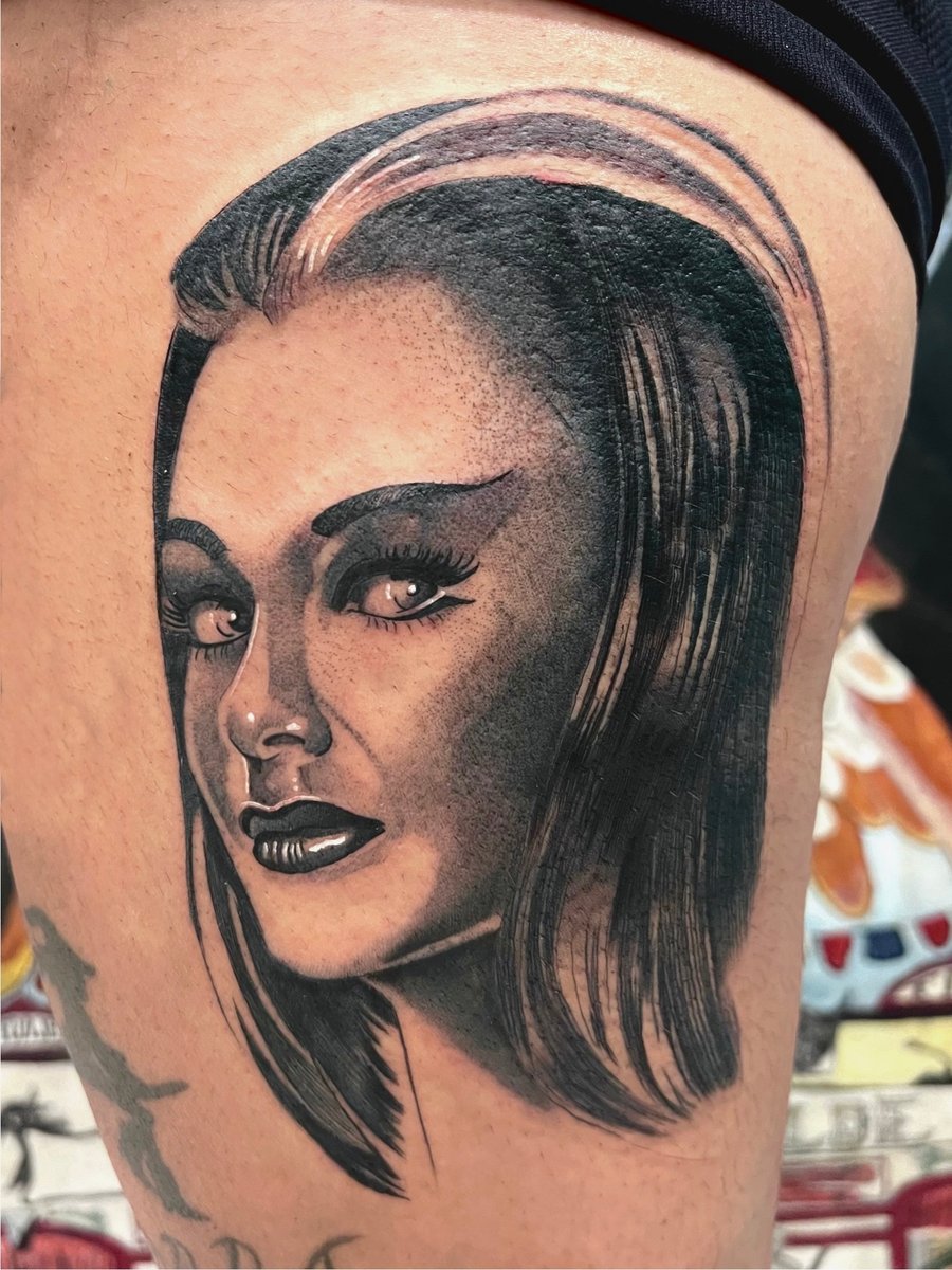 A realistic black and grey portrait of a woman's face on the thigh, showcasing detailed shading and lifelike features — by Josue Bravo, los angeles