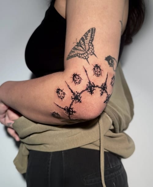 A blackwork tattoo on the outer arm featuring a geometric pattern with a butterfly design. The tattoo is bold and uses only black ink — by Shelby Bianco, los angeles