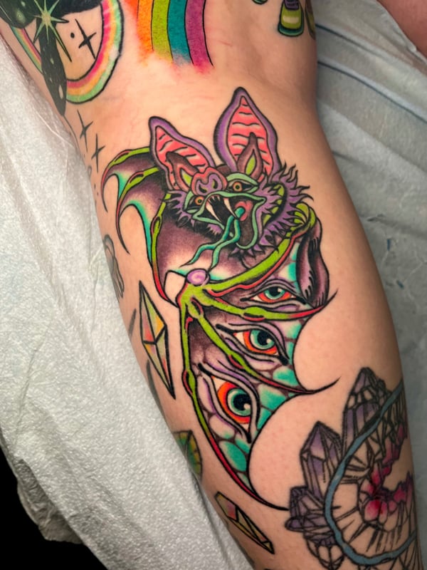 A colorful Neo-Traditional tattoo of a bat with vibrant wings on the arm, featuring bold outlines and bright colors — by Megan Rose, long beach, ca