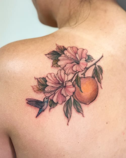 A delicate and colorful tattoo of a hummingbird with flowers and fruit on the back, featuring realistic details and a romantic style — by Melanie Benoit, los angeles