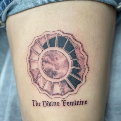 A black and grey geometric sun and moon tattoo on the thigh with 'The Divine Feminine' script underneath — by Sandra Price, los angeles
