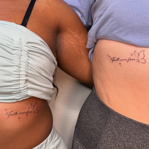 A delicate black and grey 'faith over fear' script tattoo with a butterfly on the rib, featuring fine line work — by NJ TATTOOZ, los angeles