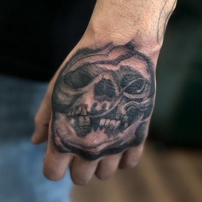 A bold black and grey skull tattoo on the hand with dark shading — by Maddie Ramirez, los angeles