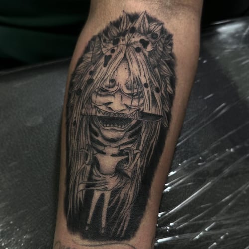 A black and grey demon face tattoo with long hair on the forearm, featuring dark and graphic elements — by Maddie Ramirez, los angeles
