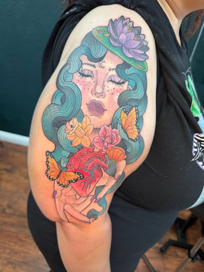 A colorful neo-traditional tattoo on the upper arm depicting a woman with flowing hair, surrounded by flowers and butterflies — by Jessica Linden, los angeles