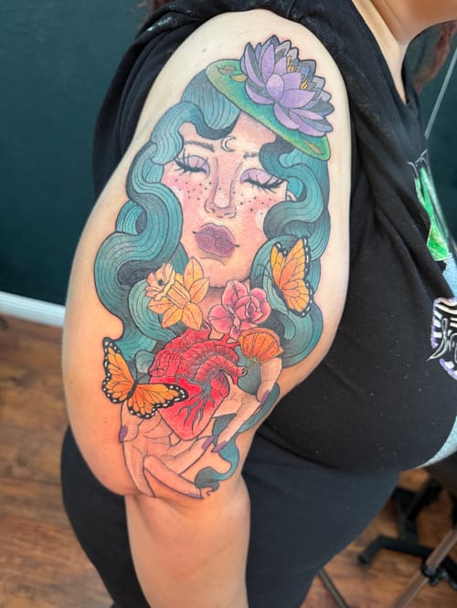 A colorful neo-traditional tattoo on the upper arm depicting a woman with flowing hair, surrounded by flowers and butterflies — by Jessica Linden, los angeles