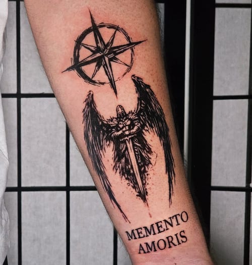 A black and grey tattoo of an angel with a sword and a compass above, accompanied by script on the forearm — by Miguel ANGELO, los angeles