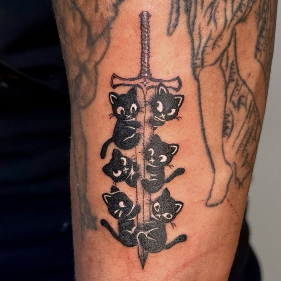 A whimsical black and grey tattoo of black cats climbing a sword on the forearm, done in an illustrative style — by NJ TATTOOZ, los angeles