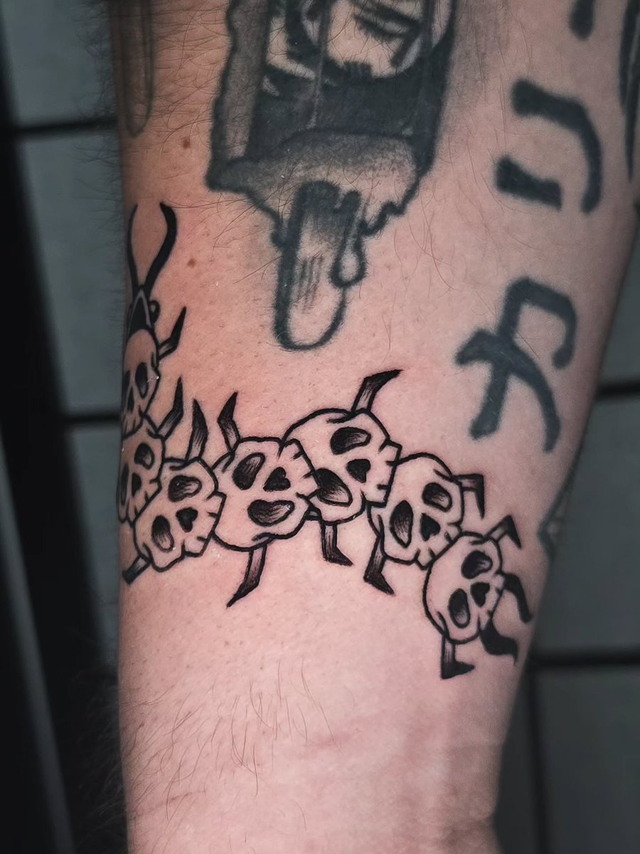 A graphic blackwork tattoo of a skull centipede on the forearm, featuring bold lines and dark shading — by Miguel ANGELO, los angeles