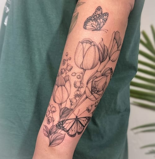 A delicate black and grey tattoo of tulips and butterflies on the forearm, featuring fine line work and clean detailing — by Melanie Benoit, los angeles