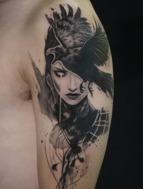 A black and grey surrealistic tattoo on the upper arm depicting a woman's face intertwined with a bird, featuring intricate shading and abstract elements — by Jian Liang, los angeles