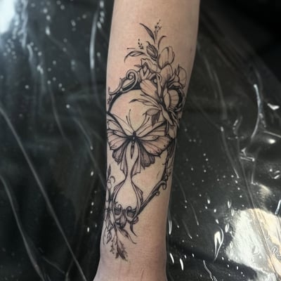 A delicate black and grey butterfly and floral design on the forearm in fine line style — by Maddie Ramirez, los angeles