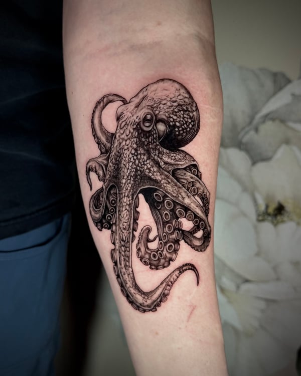A detailed black and grey realism tattoo of an octopus on the forearm, showcasing intricate shading and texture — by emily, rahway