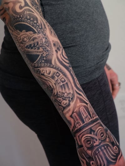 A bold black and grey tribal sleeve tattoo featuring a dragon and mask design on the arm — by Johnny Ayala, los angeles
