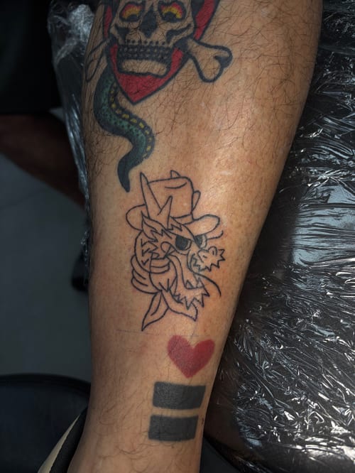 A linework tattoo of a dragon wearing a hat on the leg, accompanied by a red heart and black bars, combining traditional and linework styles — by Hannah , los angeles