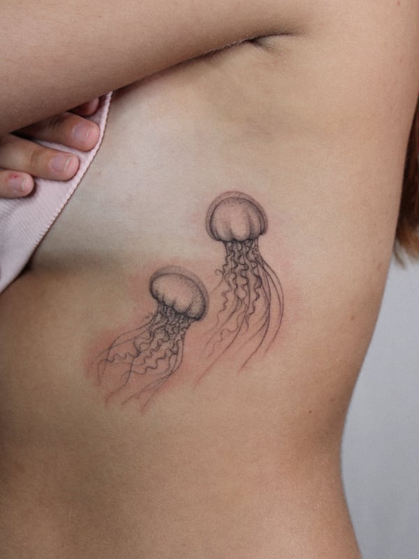 A delicate black and grey jellyfish tattoo on the rib, featuring fine line work and intricate details — by Melanie Benoit, los angeles