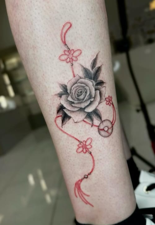 A mixed color tattoo on the calf featuring a black and grey rose with fine line red decorative elements, creating a delicate and elegant design — by otaybeatdown, los angeles