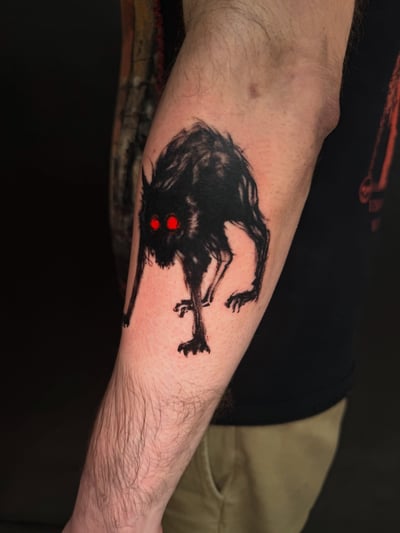 A dark blackwork tattoo of a creature with red eyes on the forearm, featuring a graphic and eerie style — by Kiera Garvin, los angeles