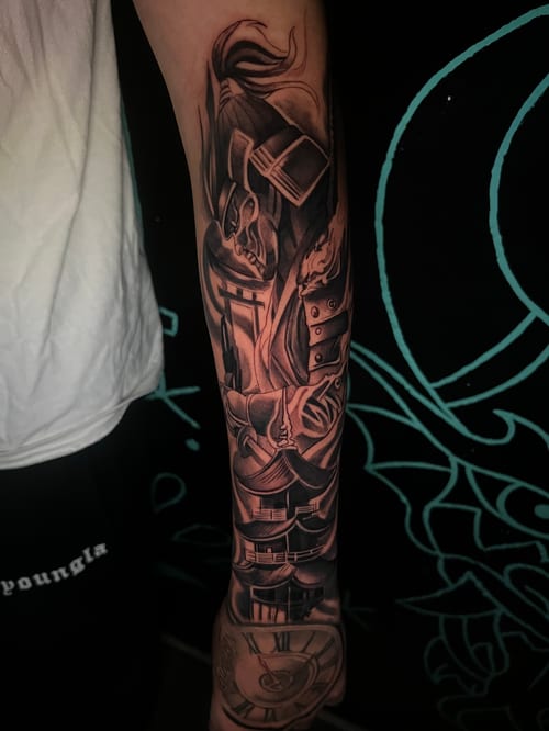 A detailed black and grey full sleeve tattoo depicting a samurai in armor with intricate shading and highlights — by Josue Bravo, los angeles