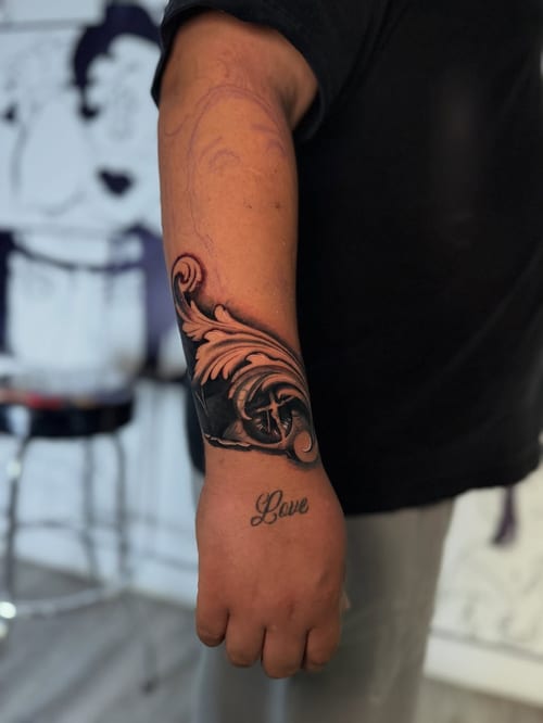 A bold black and grey compass tattoo with decorative elements on the forearm, featuring the word 'Love' in script — by zealous, los angeles