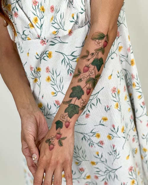 A delicate color tattoo of a strawberry vine with flowers on the forearm, featuring fine line and botanical elements — by Melanie Benoit, los angeles