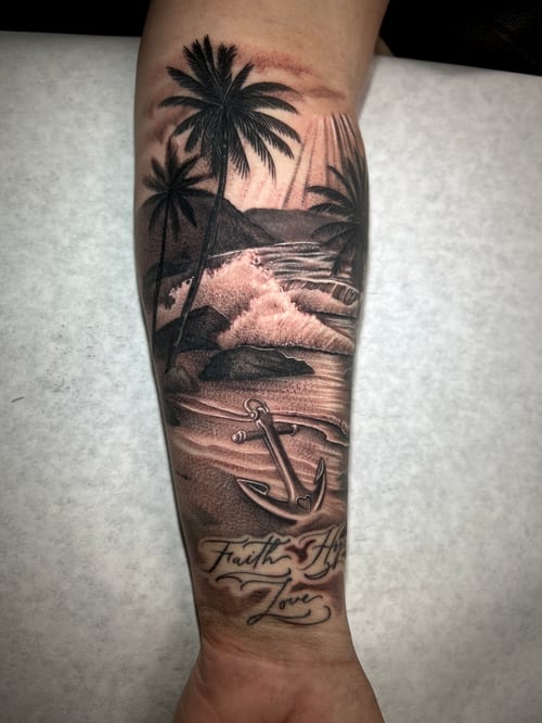A black and grey realism tattoo on the forearm depicting a tropical beach scene with palm trees, waves, and an anchor, accompanied by script text — by imindisoul, los angeles