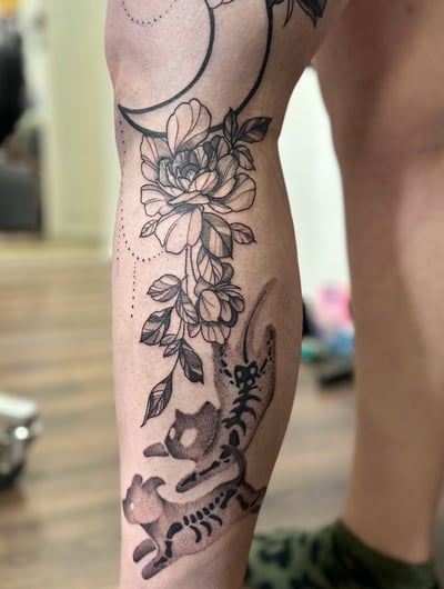 A delicate black and grey moth and floral design with a crescent moon on the thigh, featuring fine line and dotwork details — by Maddie Ramirez, los angeles