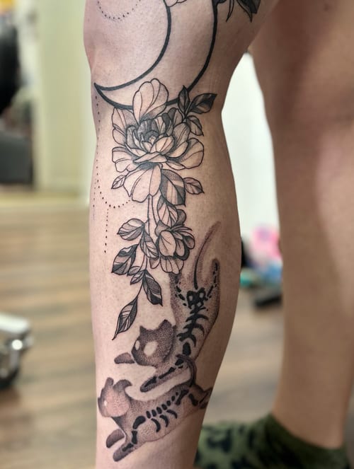 A delicate black and grey moth and floral design with a crescent moon on the thigh, featuring fine line and dotwork details — by Maddie Ramirez, los angeles