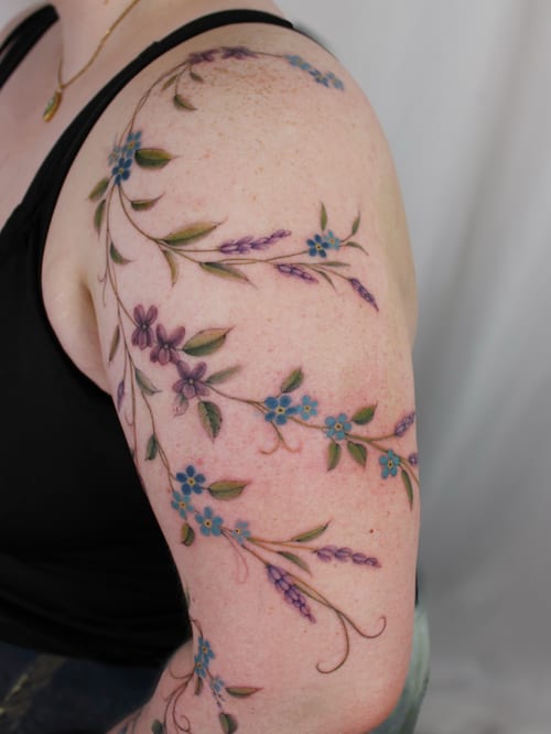 A delicate floral vine tattoo in color on the upper arm, featuring fine line work and a romantic style — by Melanie Benoit, los angeles