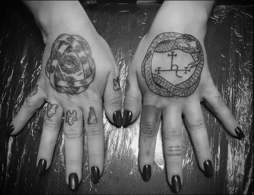 Black and grey linework tattoos on both hands featuring a snake and symbolic designs, with bold outlines and intricate details — by Tag Devilish, los angeles