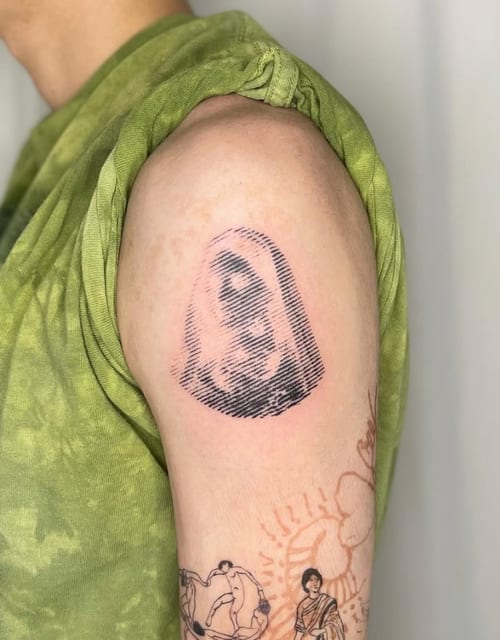 A black and grey linework tattoo on the upper arm depicting a simplistic portrait with an abstract, sketch-like appearance — by Level tattoo, los angeles