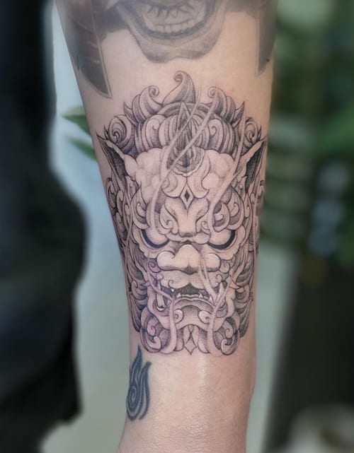 A detailed black and grey Japanese-style demon mask tattoo on the forearm, featuring intricate linework and shading — by Jian Liang, los angeles