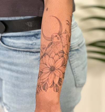 A delicate black and grey tattoo of birds and flowers on the forearm, featuring fine line work and a crescent moon — by Melanie Benoit, los angeles
