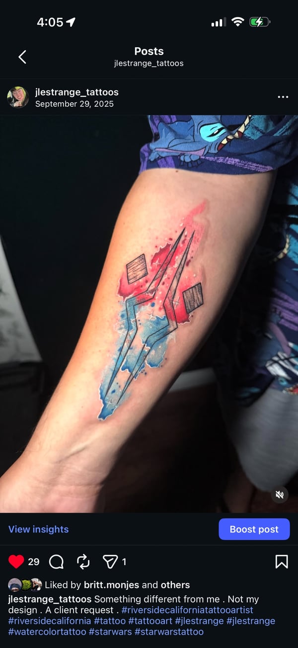 A colorful watercolor and illustrative tattoo of a stylized sword on the forearm, featuring vibrant red and blue hues with abstract elements — by Jessica Linden, riverside, ca