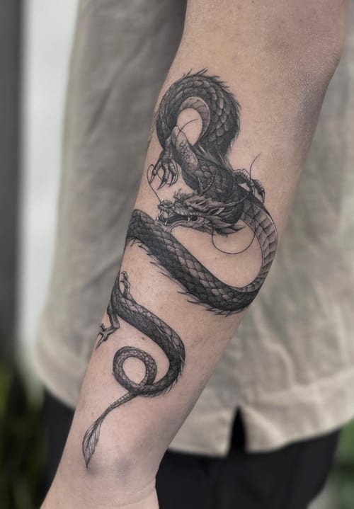 A detailed black and grey dragon tattoo on the forearm, featuring realistic scales and dynamic movement — by Jian Liang, los angeles