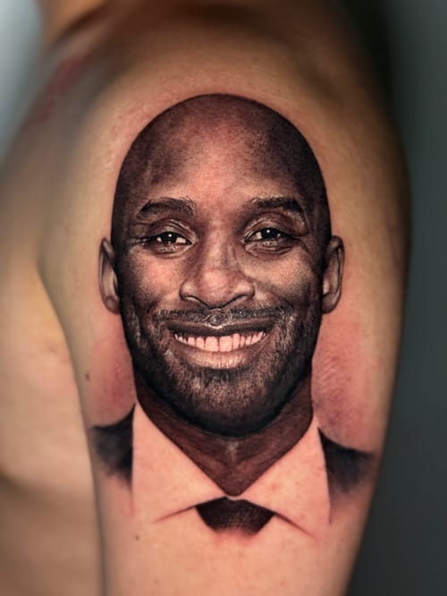 A highly detailed black and grey realism portrait of a smiling man on the upper arm — by 钟逸政, los angeles
