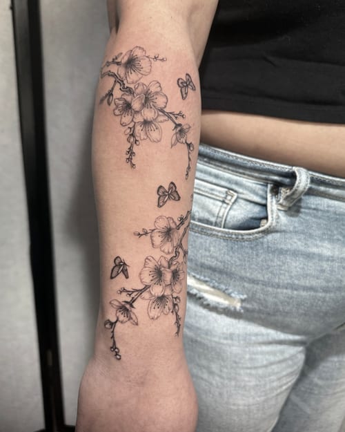 A delicate black and grey fine line tattoo of flowers and butterflies on the forearm, featuring intricate details and soft shading — by Shelby Bianco, los angeles