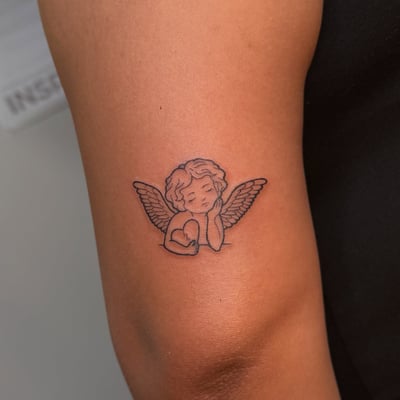 A minimalist black and grey cherub tattoo on the arm, featuring delicate linework and a small heart — by NJ TATTOOZ, los angeles