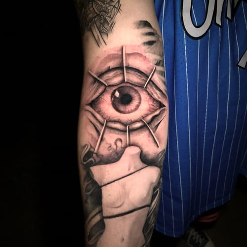 A realistic tattoo of an eye on the forearm, featuring detailed shading and a mix of color and black ink — by Travis Ross, los angeles