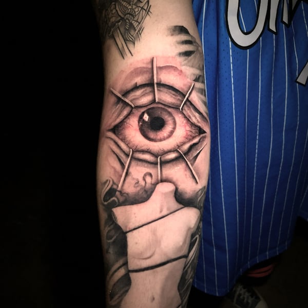 A realistic tattoo of an eye on the forearm, featuring detailed shading and a mix of color and black ink — by Travis Ross, inglewood, ca