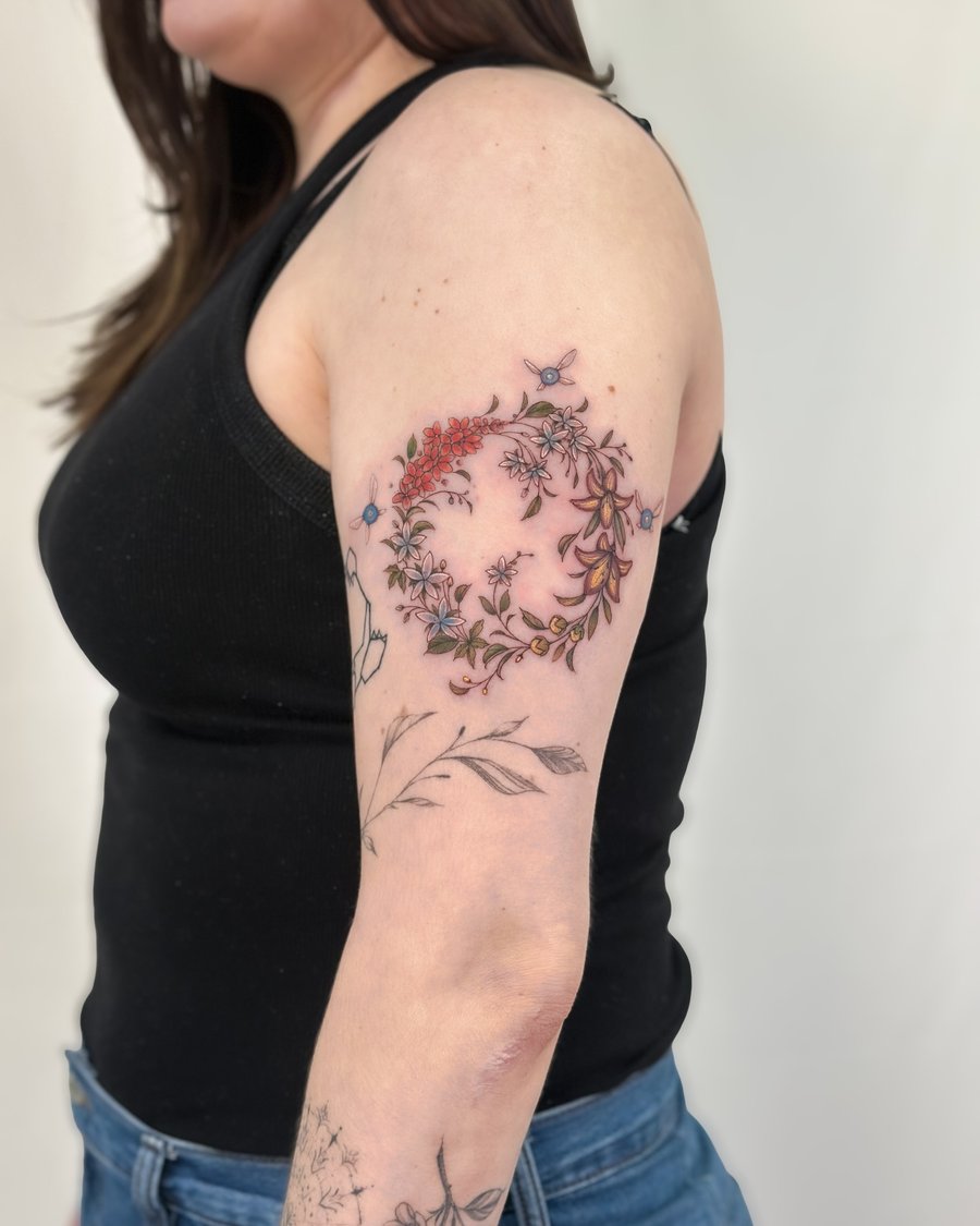 A delicate floral wreath tattoo in color on the upper arm, featuring fine line botanical elements — by Melanie Benoit, los angeles